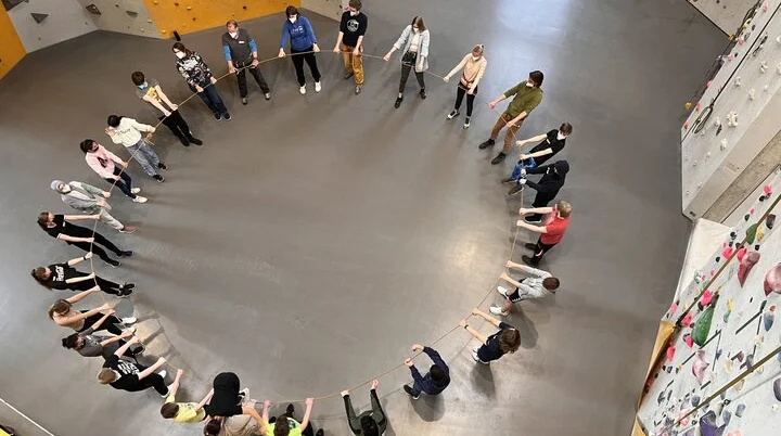 Gruppenübung im Kletterzentrum, viele Teilnehmende stehen im Kreis und halten ein Seil | © DAV Bremen